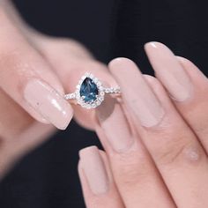 a woman's hand holding a ring with a blue stone on it and diamonds around the band