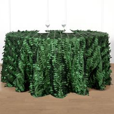 a table covered in green leaves with wine glasses sitting on top of the table next to it