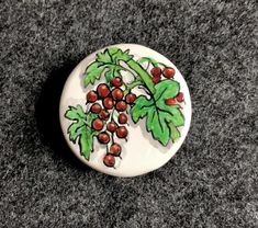 a white button with red berries on it sitting on a gray carpet next to a black floor