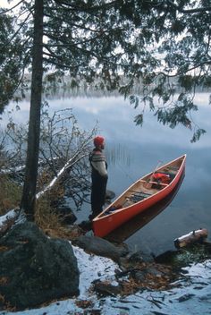 a man standing next to a red canoe on top of a lake