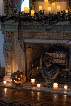 candles are lit in front of a fireplace with a statue and pumpkins on the mantle