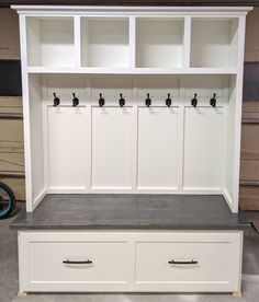 a white bench with two drawers and three black knobs on the top, next to a bike