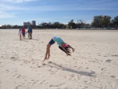 a person is doing a handstand on the beach while others are walking in the background