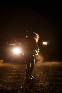 a woman is running in the dark with her arms spread out and headlight on