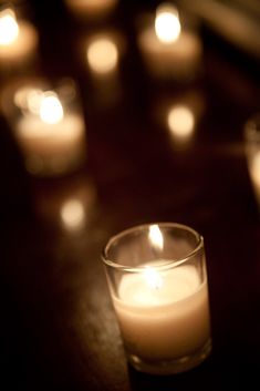 lit candles are sitting on a table in front of the glass cup that is filled with them