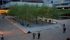 people are walking around in an open courtyard area with trees and lights on the walkway