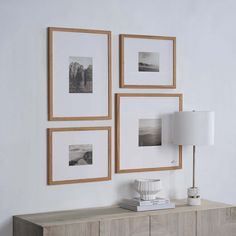 three framed pictures hang on the wall next to a dresser with a lamp and book