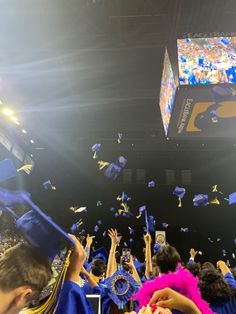 graduates throwing their caps in the air at graduation ceremony with bright lights and blue gowns