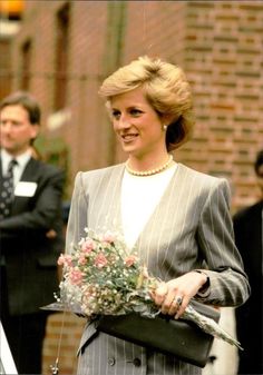 a woman in a suit holding a bouquet of flowers while standing next to other people