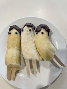 three bananas with chocolate on them sitting on a white plate