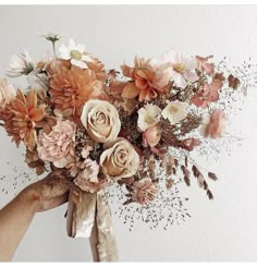 a person holding a bouquet of flowers in their hands with the background painted white and beige