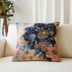 a colorful pillow on a white couch in front of a potted plant and window