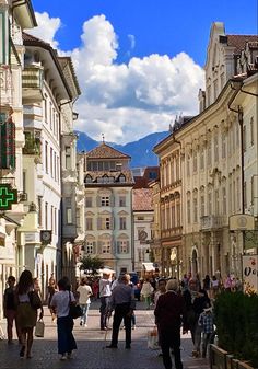 many people are walking down the street in an old european town with mountains in the background