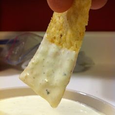 a hand holding a tortilla chip over a bowl of dip and cheese sauce