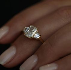 a woman's hand holding an engagement ring with a diamond in the center and two baguettes on each side