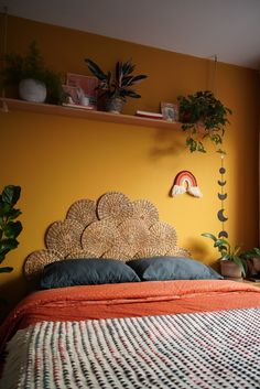 a bedroom with yellow walls and plants on the shelf above the bed, along with a wicker headboard