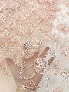 a woman's hand is covered with pearls and flowers on a pink lace background