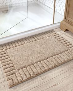 a bathroom rug on the floor in front of a shower door with a wooden cabinet next to it