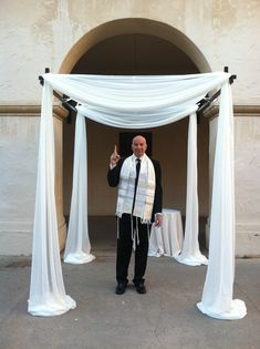 a man standing in front of a white drape with his hand up to the side