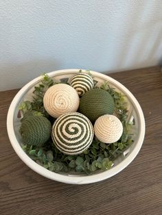 a white bowl filled with green balls and greenery on top of a wooden table