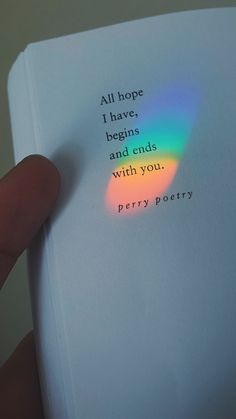 a hand holding an open book with a rainbow colored light on the cover and writing all hope i have begins and ends with you