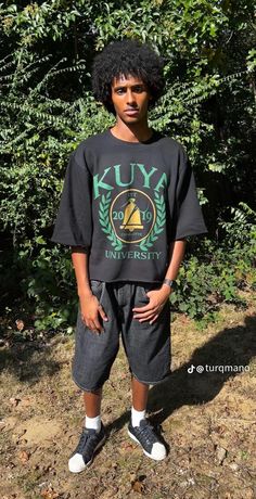 a young boy standing in front of some trees wearing a black shirt with the words kuy university on it