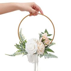 a hand holding a hoop with flowers and greenery in it, against a white background