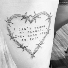 a heart shaped tattoo with barbed wire around it that says i can't drown my demons, they know how to swim