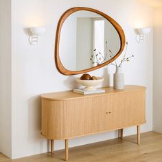 an oval mirror on the wall above a wooden dresser and vase with flowers in it