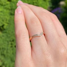 a woman's hand with a wedding ring on her finger, in front of some bushes