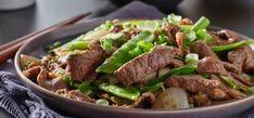 a bowl filled with meat and vegetables on top of a table next to chopsticks