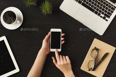 a person using their cell phone while sitting at a desk in front of laptops