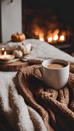 a cup of coffee sitting on top of a blanket next to a fire in the fireplace