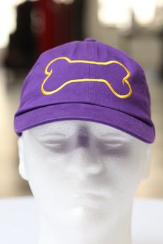 a white mannequin head wearing a purple hat with a yellow bone on it