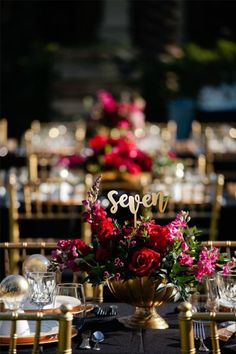 the table is set with gold chairs, plates and flowers in vases on them