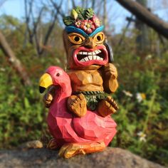 a wooden carving of a totema holding a flamingo on top of a rock