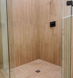 a walk in shower sitting next to a tiled wall and wooden paneled flooring