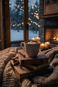 a cup of hot chocolate sits on top of two books in front of a fireplace