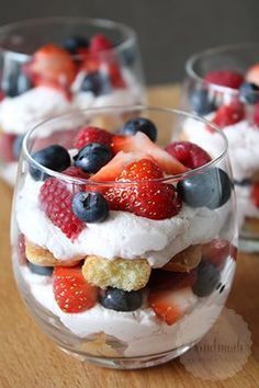 small desserts are arranged in glass bowls on a wooden counter top, with berries and whipped cream