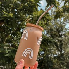 a person holding up a drink with a straw in it's hand and trees in the background