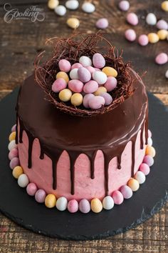 a chocolate cake covered in candy eggs on top of a black plate with pink icing