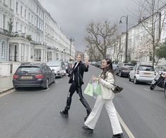 two women walking down the street in front of parked cars and buildings on a cloudy day