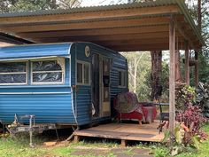 a blue trailer parked in front of a wooden deck under a covered area with furniture