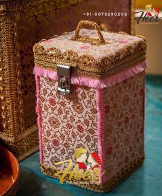 a pink and gold box sitting on top of a blue table next to a vase