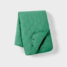 a green quilted blanket folded on top of a white wall