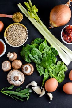 an assortment of food including mushrooms, spinach, eggs and broccoli on a black surface