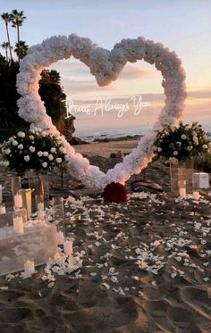 a heart shaped arrangement on the beach with candles and flowers