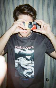 a young man taking a photo with his cell phone while wearing a t - shirt