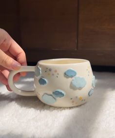 a hand holding a coffee cup with blue clouds on it and white furnishing