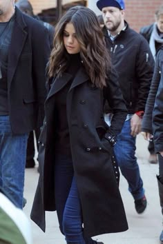 the woman is walking down the street in her black coat and jeans, with other people behind her